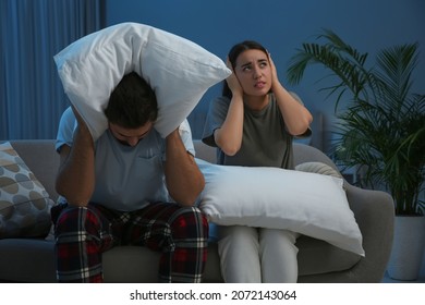 Young Couple With Pillows Suffering From Noisy Neighbours In Living Room At Night