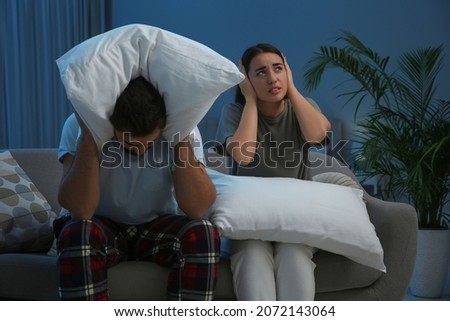 Young couple with pillows suffering from noisy neighbours in living room at night Foto d'archivio © 