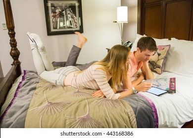 Young Couple Planning Their Trip And Adventures. Lying On The Bed With A Map And An Ipad