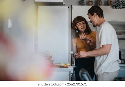 A young couple playfully interacts while preparing food in the kitchen. They are laughing and enjoying their time together in a cozy home environment.