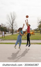 young couple playing basketball. Man jumping to throw the ball to the basket. Woman defending, blocks shot. Entertainment in public park, outdoors.