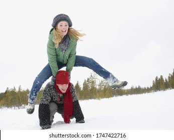 A Young Couple Playing Leap Frog In The Snow