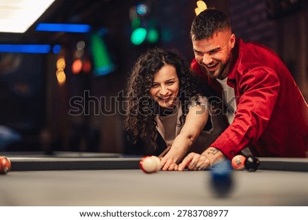 Young couple playing pool, sharing a laugh and enjoying a playful date night in a vibrant club environment