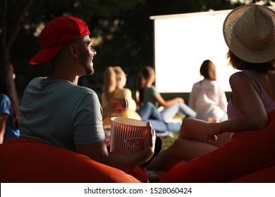 Young couple with popcorn watching movie in open air cinema. Space for text