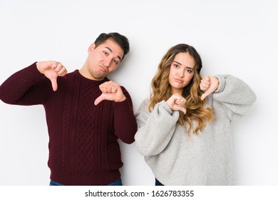 Young couple posing in a white background showing thumb down and expressing dislike.