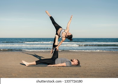 Young couple practicing acroyoga exercises in the evening on the beach over sea background - side star 