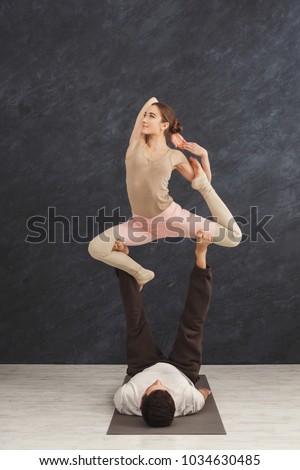 Young couple practicing acroyoga on mat in gym together. Woman balancing on man legs. Partner yoga, flexibility, trust concept, copy space