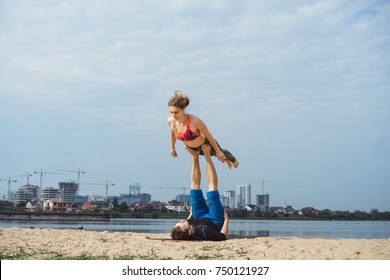 young couple practicing yoga outdoors on a city background. A girl with dreadlocks practicing hatha yoga on the shore of a lake, in the distance a big city. pair yoga man and woman, fly yoga - Powered by Shutterstock