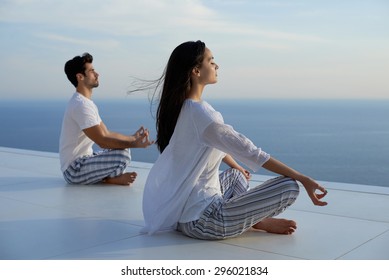 young couple practicing yoga at sunset in modern home terace with ocean and sunset in background - Powered by Shutterstock