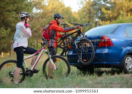 Young Couple Preparing for Riding the Mountain Bikes in the Forest. Unmounting the Bike from Bike Rack on the Car. Adventure and Family Travel Concept.