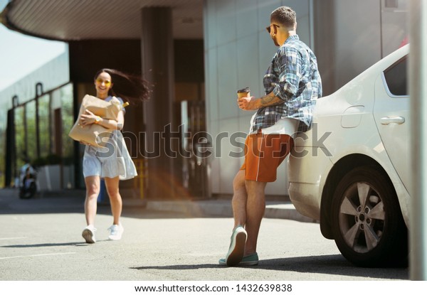 Young couple preparing for vacation trip on the\
car in sunny day. Woman and man shopping and ready for going to\
sea, riverside or ocean. Concept of relationship, vacation, summer,\
holiday, weekend.