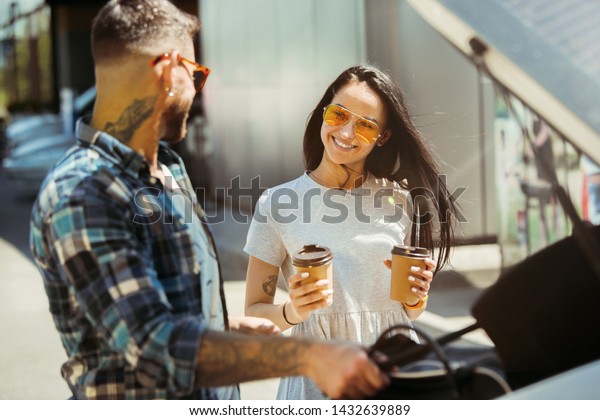 Young couple preparing for vacation trip on the\
car in sunny day. Woman and man drinking coffee and ready for going\
to sea or ocean. Concept of relationship, vacation, summer,\
holiday, weekend.