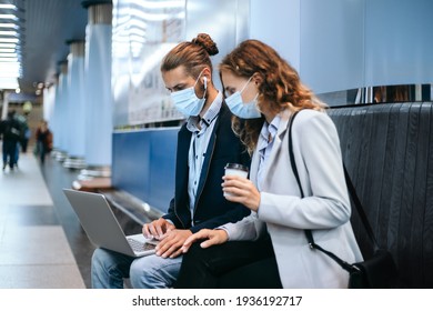 Young Couple In Protective Masks Using A Laptop On The Subway Platform .