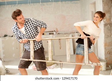 Young couple pulling ladder to opposite directions in house under construction, having fun.