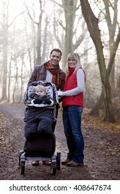 A Young Couple Pushing A Stroller In The Park, Smiling