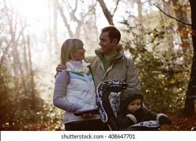 A Young Couple Pushing A Stroller In The Park, Smiling