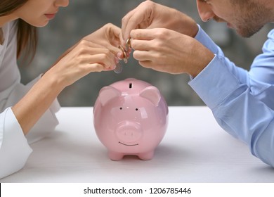 Young couple putting money into piggy bank on table