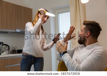 young couple in a quarrel women attack man with meat knife standing in the kitchen. she found his mobile phone with message from a potencial lover. act of jealousy.