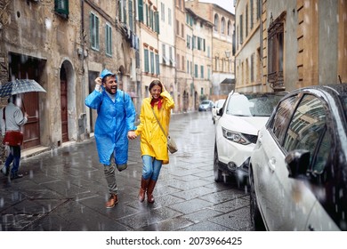 A Young Couple In Raincoats On The Street Is Running To Hide From The Rain In A Hurry Atmosphere. Walk, Rain, City, Relationship