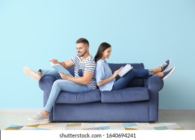 Young Couple Reading Books While Sitting On Sofa At Home