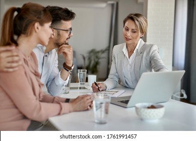 Young Couple And Real Estate Agent Communicating About Housing Plans While Using Computer During A Meeting. 