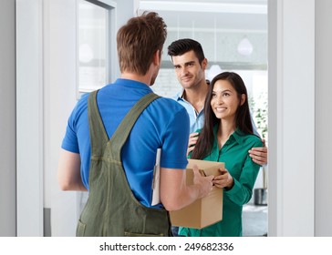 Young Couple Receiving Package From Delivery-man At Home.