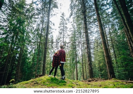 Young couple in red shirts stand on the moss in the woods and hugging on while walking. Woman and man spend time together in a mountain forest.