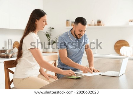 Young couple with refund form using calculator in kitchen