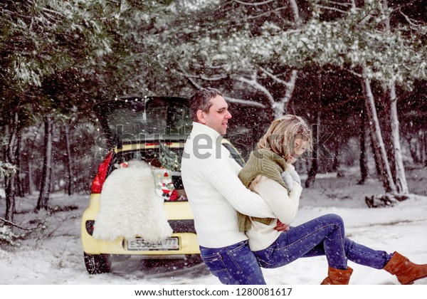 young couple in relationship hugging near yellow
car , wearing white sweaters and blue jeans. Man roolls his woman
on hands. The weather is snow
