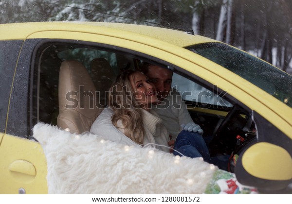 young couple in relationship\
hugging in yellow car , wearing white sweaters and blue jeans.\
