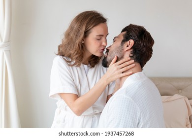 Young couple in a relationship kissing and cuddling. Happy couple hug and kiss on the bed near the window in the morning. Sensual young couple kissing on bed at home. 