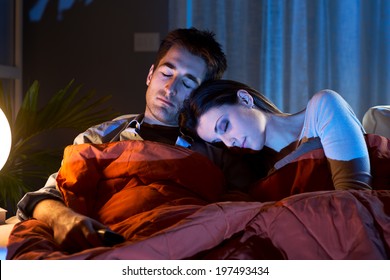Young couple relaxing at home with blanket in front of TV.