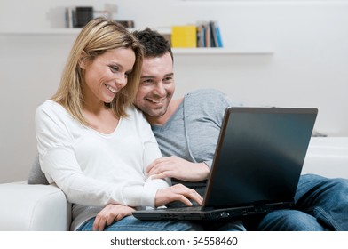 Young Couple Relaxing On The Couch With Laptop In Their Living Room At Home