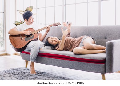 Young couple relaxing on sofa in living room.Handsome man playing guitar on sofa and a beautiful woman lying down on sofa. Asian girlfriend hands playing near to her boyfriend.  - Powered by Shutterstock