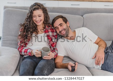 Young couple relaxing in their apartment, lying on the couch and watching the movie. The lens is the effect of glare on the window.