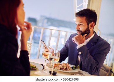 Young Couple At Restaurant Having Dinner. Man Using Mobile Phone
