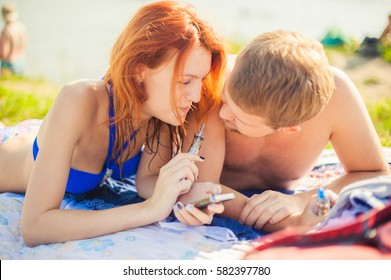 young couple resting on the beach, smoking electronic cigarette