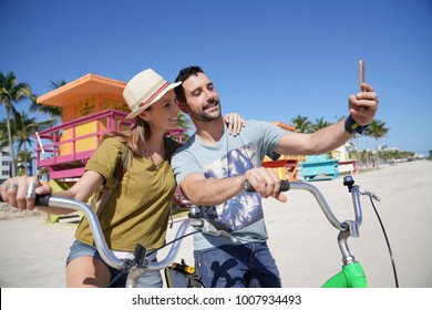 Young couple riding bikes in Miami beach, taking selfie pictures  - Powered by Shutterstock