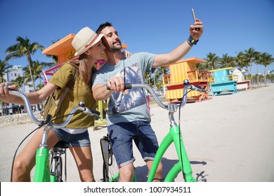 Young couple riding bikes in Miami beach, taking selfie pictures  - Powered by Shutterstock