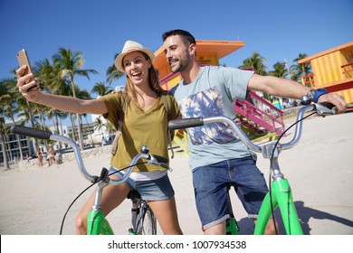 Young couple riding bikes in Miami beach, taking selfie pictures  - Powered by Shutterstock