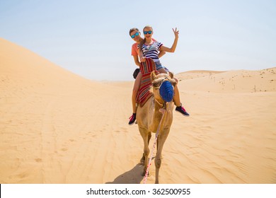 Young Couple Riding A Camel In The Middle Of A Desert Near Emirates On Their Wedding Day