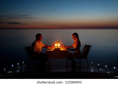 A young couple with a romantic dinner with candles on the sea sand beach