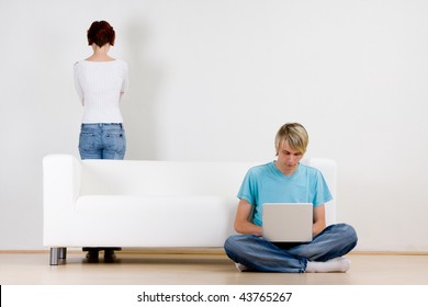 Young Couple In Room With Man On Laptop And Woman Standing Behind Couch.