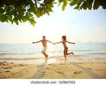 Young Couple Running On A Sandy Beach At Sunset