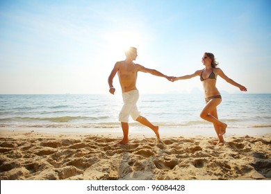 Young Couple Running On A Tropical Beach At Sunset