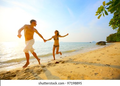 Young Couple Running On A Tropical Beach At Sunset