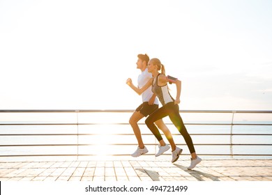 Young Couple Running Over Wooden Pier At Sunset