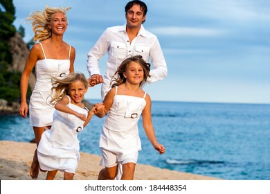 Young Couple Running Together With Kids On Beach.