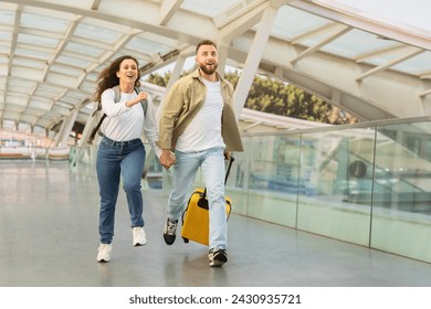 Young couple in rush running with yellow suitcase at the airport, happy millennial man and woman laughing and enjoying the start of their vacation, rushing to flight boarding, copy space - Powered by Shutterstock