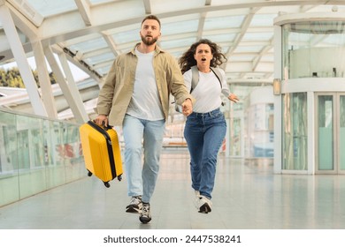 A young couple rushes through an airport terminal, urgency etched on their faces, with luggage in tow.
